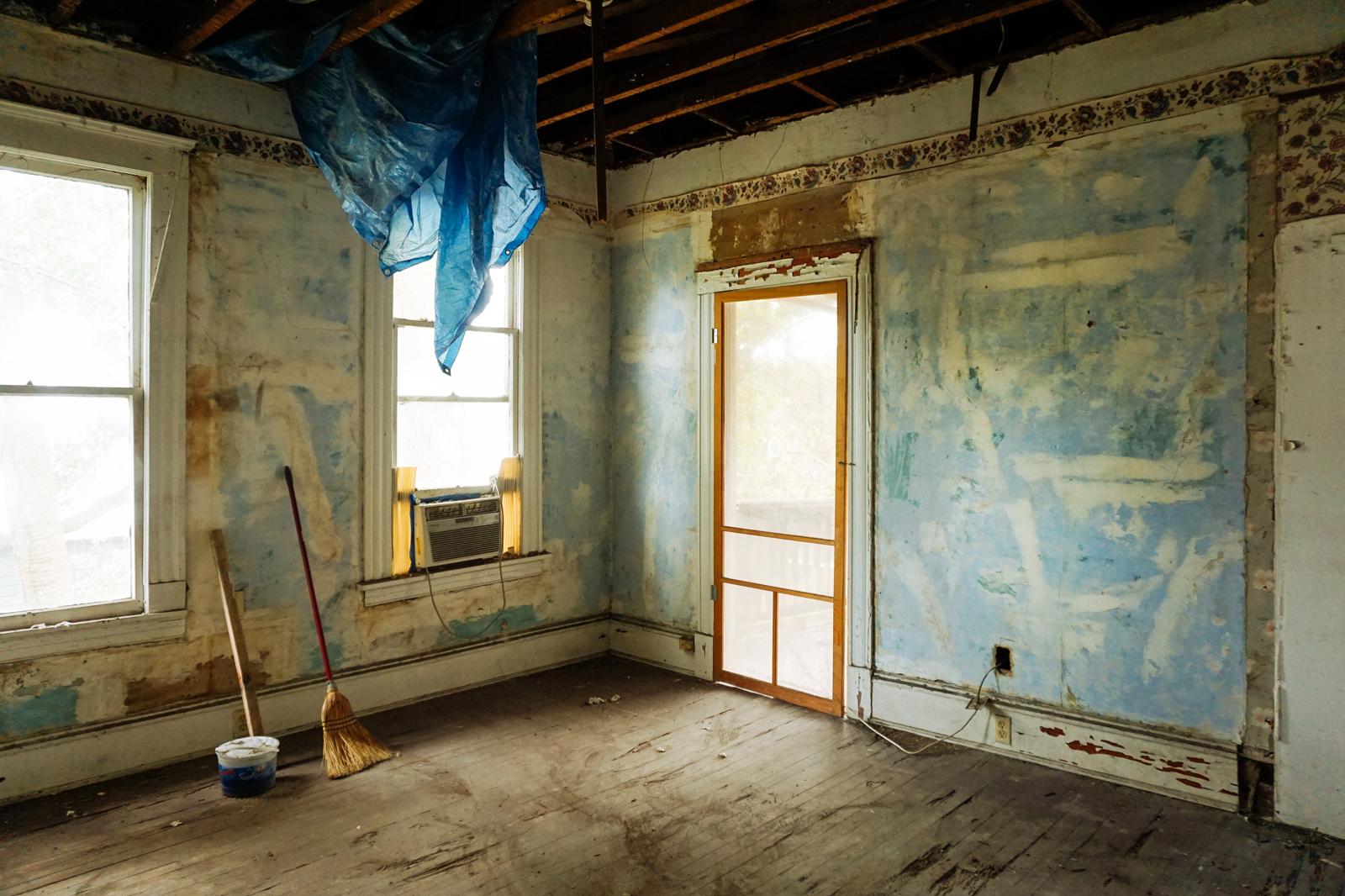 Room stripped back with peeling wallpaper and exposed ceiling joists before refit