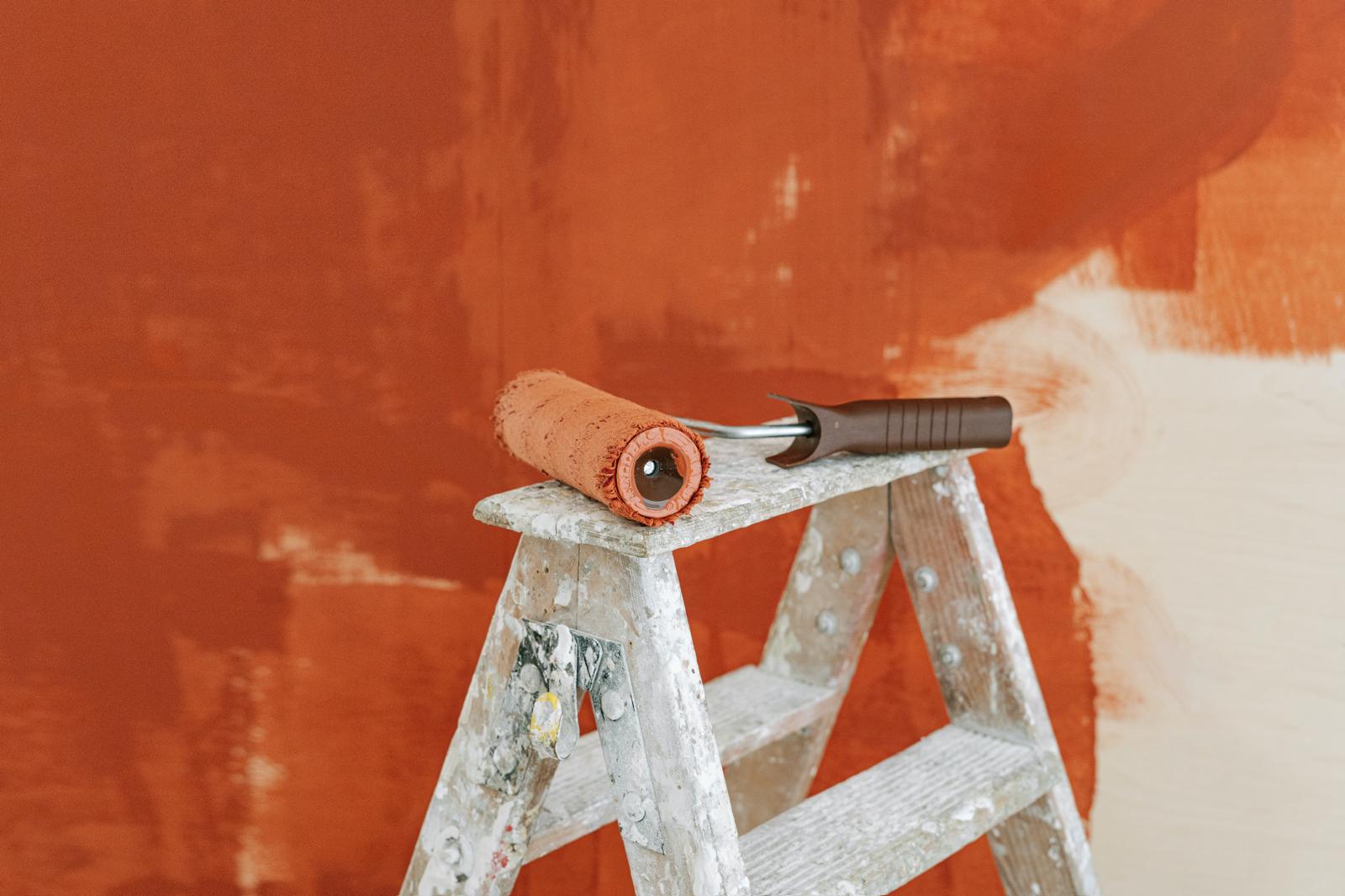 Paint roller on a stepladder against a freshly painted terracotta wall