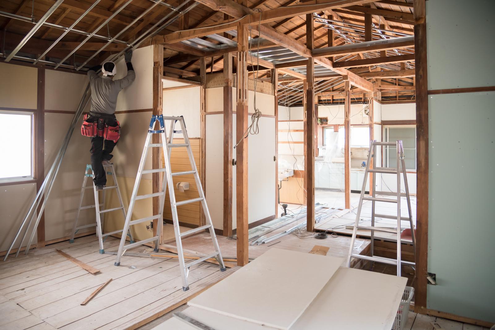 House interior with exposed timber framing while worker installs ceiling panels